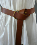 A man's brown leather ring belt with brass ring belting a white tunic.