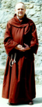 A man in a rust brown monk's robe with hood and rope belt..