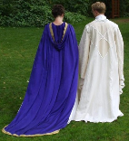 A couple dressed in custom-made wedding garb consisting of a long purple cloak with gold trim and train and a white replica Saruman wizard's robe.